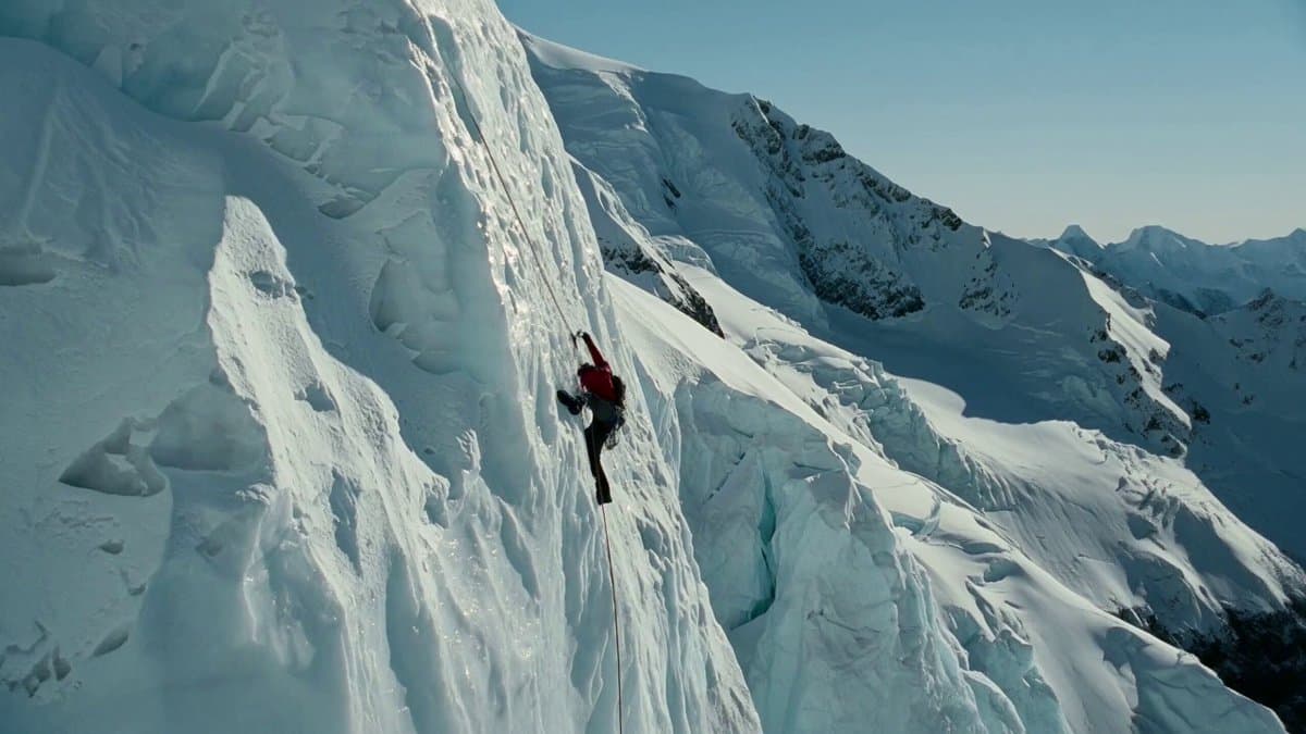 A rugged climber dangles precariously from a sheer ice cliff, their frost-covere